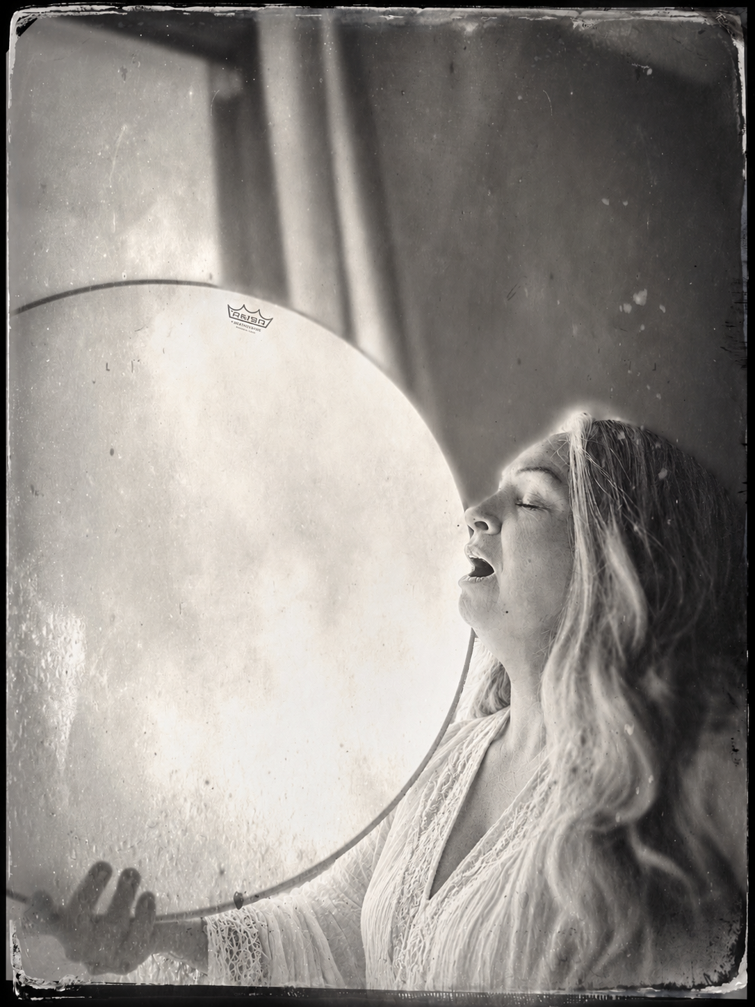 Joya Sosnowski in profile, singing with a frame drum lifted toward the light
